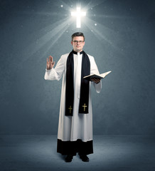 A young caucasian priest with deep faith blessing with the holy bible in his hand in front of blue...