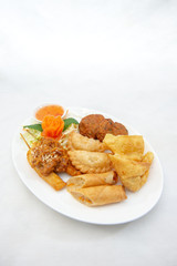 Mixture of Thai appertizers with deep-fried spring rolls, curry puffs, wontons, fish cakes and chicken satay skewers