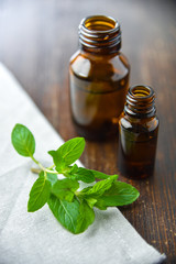 Essential oil of peppermint in a small brown bottle with fresh green mint on an old wooden background, selective focus