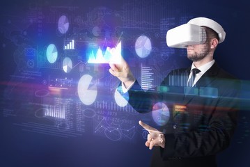 Elegant businessman in DJI goggles handling 3D reports and charts around him
