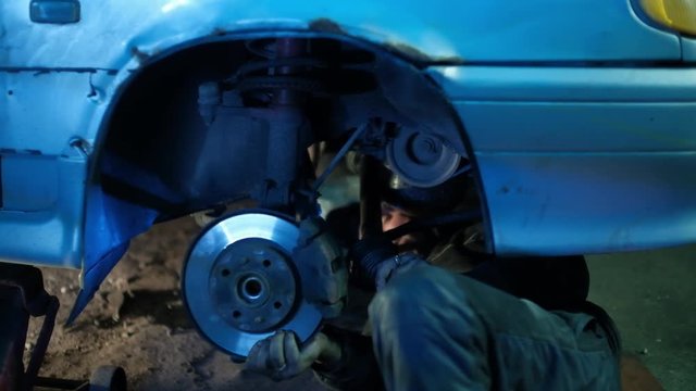 The mechanic in dirty auto repair shop repairs the car - repairs constant-velocity universal ball joint Shrus and replaces a wheel
