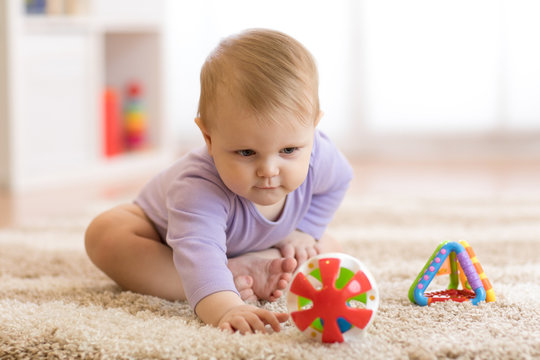 Baby girl playing with colorful toys sitting on a carpet at home