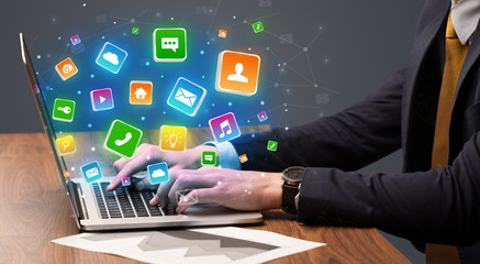Businessman hand typing on laptop with flying application icons around

