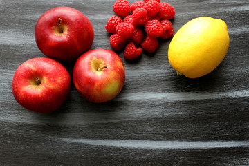 Apples, group of raspberries and lemon on shabby painted, black and blue board, top view, copy space