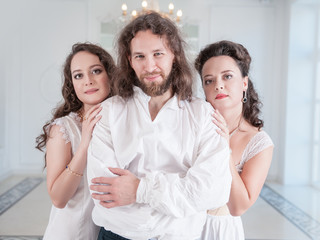 Man in medieval costume and two beautiful woman in old-fashioned negligee