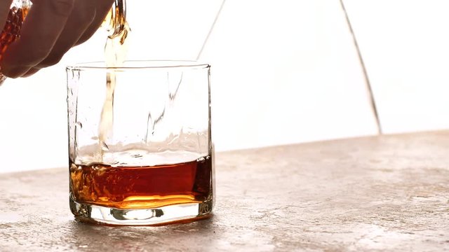 Pouring whiskey into a glass on old wooden table and light blurred background.