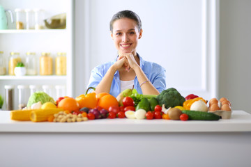 Young and cute woman sitting at the table full of fruits and vegetables in the wooden interior