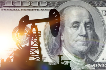 silhouette of an oil drilling pump on a hundred dollar background. oil business, market and prices for oil barrel