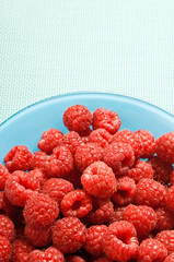fruit red raspberries in blue bowl over blue background with copy space 