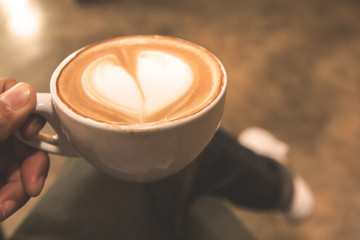Hand holding cup of hot coffee in cafe with light in the morning