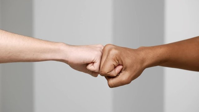 Hands gesture of two multiethnic men bumping fists closeup, isolated over white background in slow motion, friendship and greeting concept