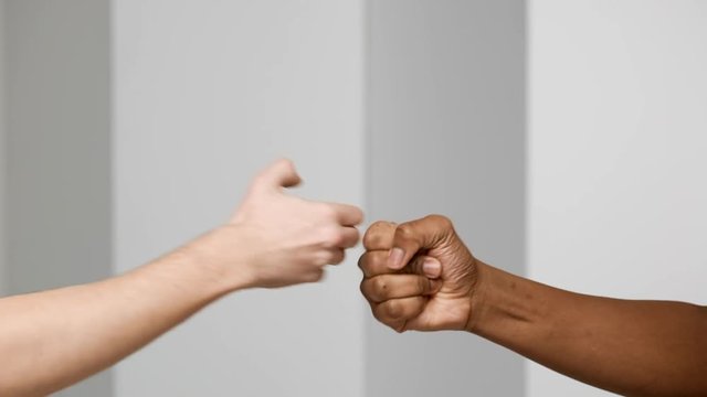 Two multiethnic men bumping fists and slapping hands closeup, isolated over white background in slow motion, friendship and greeting concept