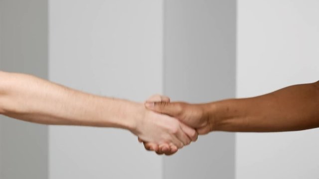 Two multiethnic men handshaking closeup, isolated over white background in slow motion, greeting or deal concept