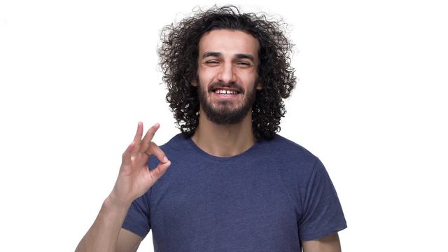 Portrait of satisfied guywith dark locks and mustach wearing casual clothing and showing ok or alright symbol, over white background. Concept of emotions