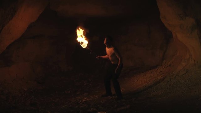 Careful hermit with burning torch in hand walks and looks around in stone cave