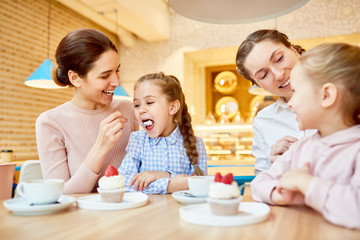 Obraz na płótnie Canvas One of young mothers feeding her daughter with dessert while spending leisure in cafe with their friends