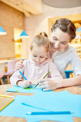 Fototapeta premium Young mother helping her daughter to draw while spending leisure in cafe