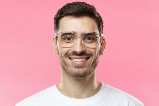 Close up portrait of smiling handsome man in trendy glasses and white t-shirt isolated on pink background