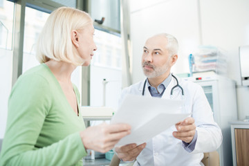 Confident clinician and his patient discussing medical papers or prescriptions during appointment