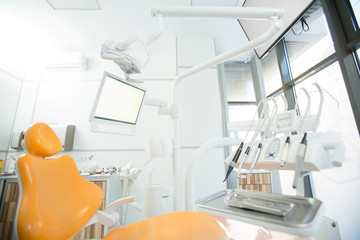 Sterile instruments for dental check-up on metallic tray, set of electric drills, display, lamp and armchair in office of dentist