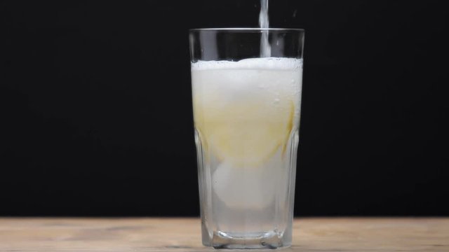 glass with ice and lemon slice on black background with homemade lemonade pouring in it