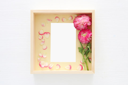 Image of delicate pastel pink beautiful flowers arrangement and empty vintage photo frame over white wooden background. Flat lay, top view. For photography mockup montage.