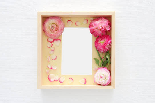 Image of delicate pastel pink beautiful flowers arrangement and empty vintage photo frame over white wooden background. Flat lay, top view. For photography mockup montage.