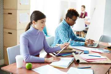 Young students in casualwear sitting in library of their college or university and preparing schoolwork
