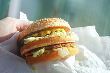 Big juicy burger with cheese in the hand with lens flare closeup
