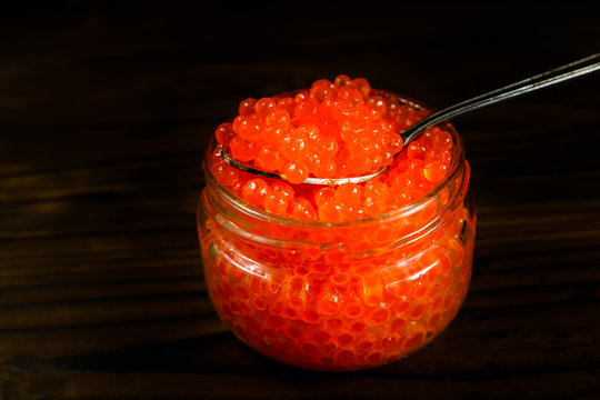 Red caviar in a spoon above the glass jar
