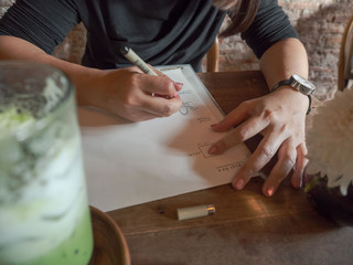 hands young female sketching drawing or writing in coffee shop on wooden table with greentea and tea on vintage look