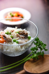Chicken fricassee with green pea served with boiled rice on a wooden background.