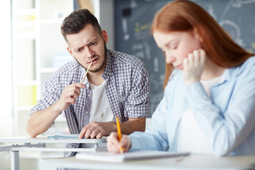 Guy looking at his groupmate notes while writing individual exam test at lesson