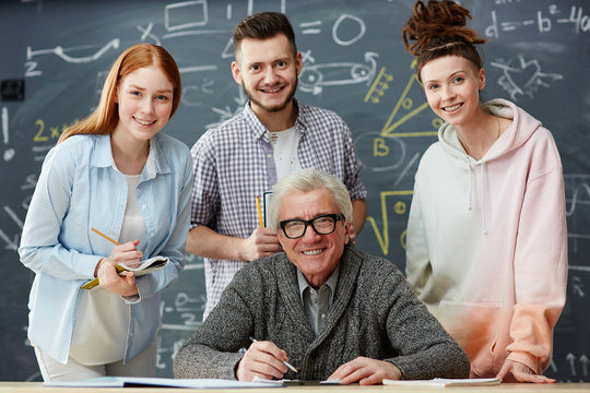 Happy professor and his successful students looking at camera on background of blackboard in classroom