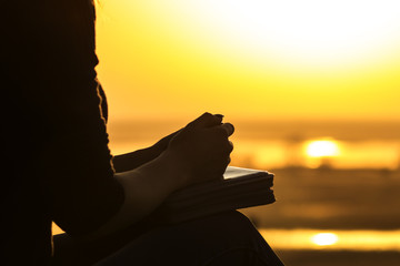 silhouette of the hands of woman praying to God in the nature witth the Bible at sunset, the concept of religion and spirituality - obrazy, fototapety, plakaty