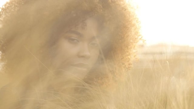 full of sunset sun portrait of black mixed race woman sits on lawn with high hay grass