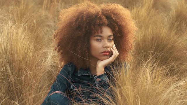 total denim look woman sits on autumn lawn field with high hay grass and looking at camera smiling then