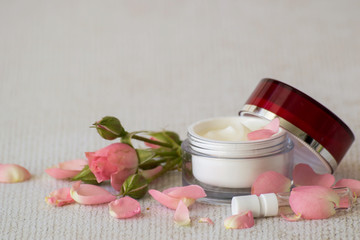 Fototapeta na wymiar Natural cosmetic. Fresh delicate petals of roses, a small round jar with cream for skin care face and a small bottle of essential oil on a light background. 