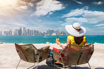 Weibliche Touristin genießt ein Getränk vor der Skyline von Doha, Katar, an einem sonnigen Tag