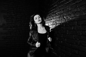 Studio portrait of sexy brunette girl in black leather jacket against brick wall.