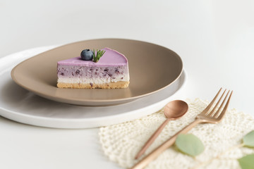 piece of blueberry cheesecake on brown ceramic plate with fork and spoon on white table