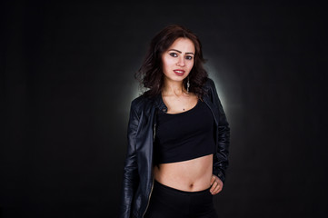 Studio portrait of sexy brunette girl in black leather jacket against black background.