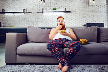Funny man eating a burger on the couch