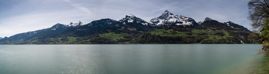 panorama view of a beautiful turquoise mountain lake panorama with snow-covered peaks and green meadows and forests