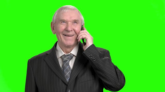 Old businessman talking on phone. Portrait of senior businessman in suit talking on phone, green hroma screen background.