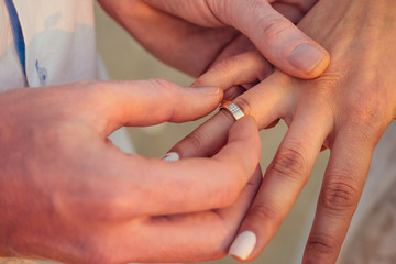 the bridegroom puts on a bride's finger a wedding ring on the beach