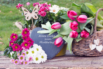 Schieferherz mit Text "Alles Liebe zum Muttertag" mit Tulpen auf Holzbrett im Garten