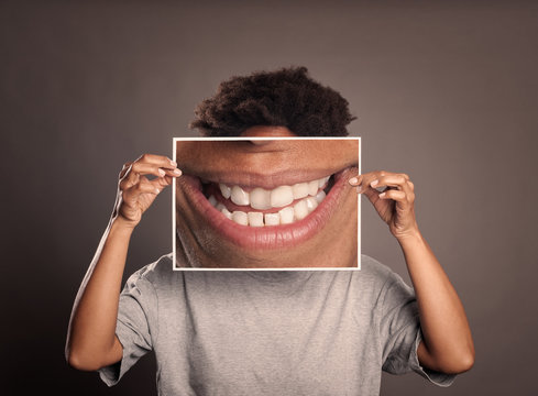 black woman holding a picture of a mouth smiling on a grey background