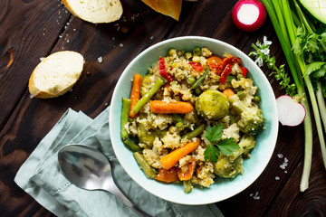 Healthy dietary vegan dish: couscous and vegetables (string beans, brussels sprouts, carrots, sweet peppers, tomatoes) on a dark rustic wooden kitchen table. Top view flat lay background.