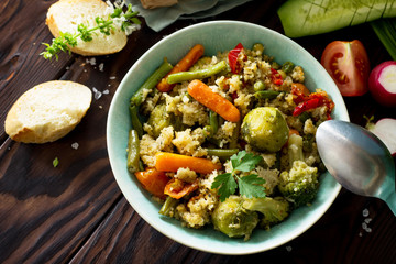 Healthy proper nutrition. Homemade vegetarian couscous with string beans, brussels sprouts, carrots, sweet peppers and tomatoes on a dark rustic wooden kitchen table. Copy space.